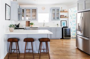 Small kitchen with white countertops and gray-blue cabinets near stainless steel refrigerator