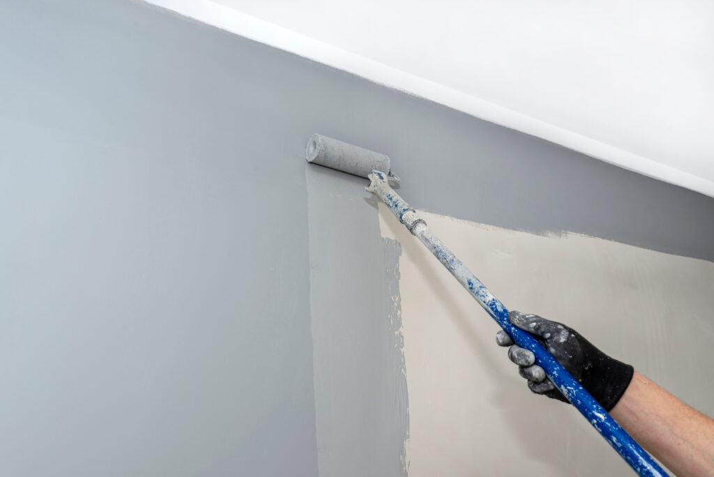 Picture of a painter rolling grey paint onto wall 