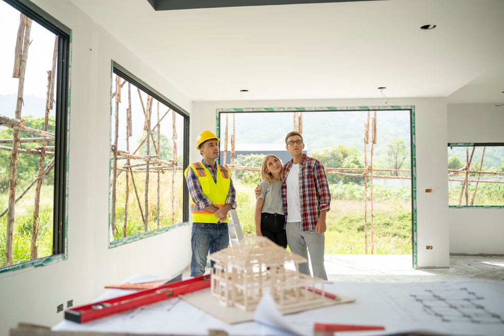 young couple and their agent examining blueprints at construction site